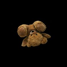 a brown teddy bear laying on its back with it's head up against the black background