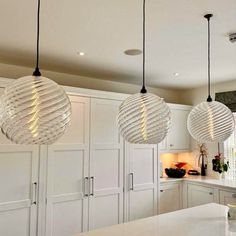 three lights hanging from the ceiling above a kitchen island with white cabinets and counter tops