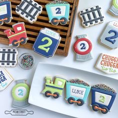 some cookies that are on a plate and next to a tray with train themed cookies