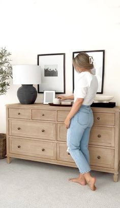 a woman standing on top of a dresser next to a potted plant and framed pictures