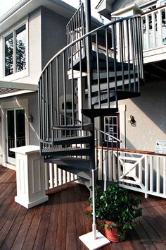 a spiral staircase in front of a house with potted plants on the deck area