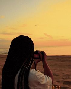 a woman with dreadlocks taking a photo on the beach at sunset or sunrise