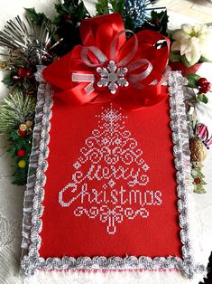 a cross stitch christmas tree on a red and white cloth with silver trimmings