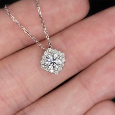 a woman's hand holding a necklace with a large diamond in the shape of a flower