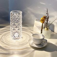 a glass vase sitting on top of a table next to a cup and saucer