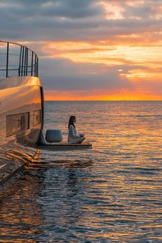 a woman sitting on the back of a boat in the ocean at sunset or sunrise