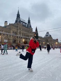 a woman in red jacket skating on ice rink next to large building with christmas lights