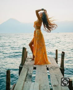 a woman in a yellow dress standing on a dock with her hair blowing in the wind