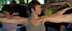 a group of people doing yoga in a room with one woman stretching her arms out