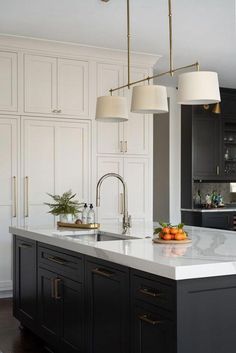 a kitchen with black cabinets and white counter tops, gold trimmings and pendant lights hanging from the ceiling