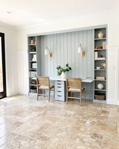 two chairs and a table in a room with shelves on the wall behind them,