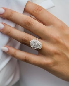 a woman's hand with a diamond ring on her finger and white shirt in the background