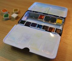 an artist's watercolor palette in its case on a table with other paints