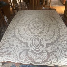 the table is covered with an intricately designed white lace fabric and has wooden chairs around it