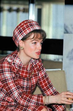 a woman sitting at a table with a wine glass in her hand and wearing a red plaid coat