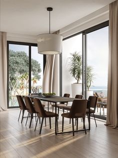 a dining room table with chairs and a lamp hanging from the ceiling next to large windows