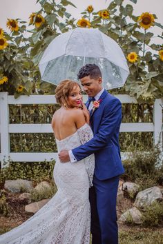 a bride and groom pose under an umbrella in front of sunflowers at their wedding