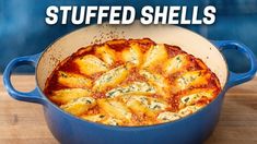 a blue casserole dish filled with stuffed shells on top of a wooden table