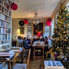 a group of people sitting at a table in front of a christmas tree with bookshelves