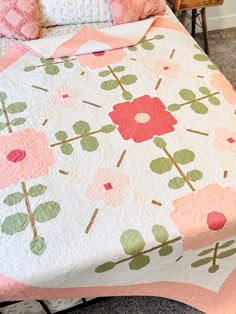 a bed with a pink and green flower quilt on it's cover, next to a chair