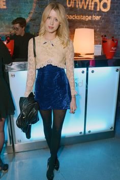 a woman standing in front of a counter wearing a blue skirt and lace top with black tights