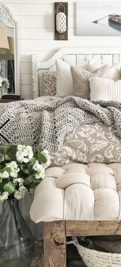 a bed with pillows and blankets on top of it next to a vase filled with flowers