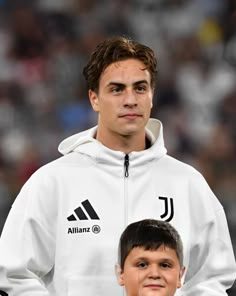 a young man holding a soccer ball next to an older man wearing a white jacket