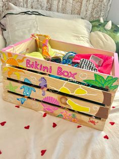 a wooden box filled with toys sitting on top of a white bed covered in pillows