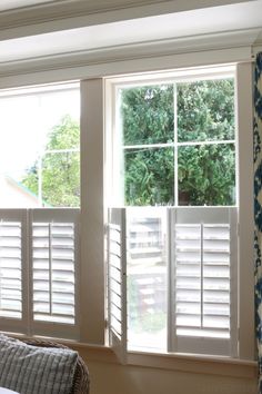 two windows with white shutters in a bedroom next to a window covered in blue and white wallpaper