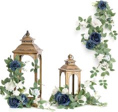 two gold lanterns with blue roses and greenery around them on a white background, surrounded by green leaves