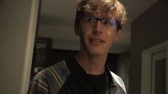 a young man wearing glasses standing in front of a mirror