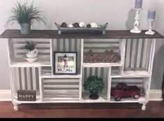 a white shelf with pictures and plants on it in front of a gray striped wall