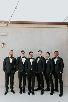 a group of men in tuxedos standing next to each other near a wall