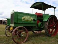 an old fashioned green and red tractor on display in a field with other farm equipment