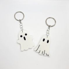 two white ghost keychains with black eyes and hands on each side, one is holding