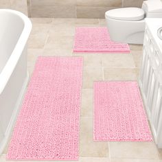 three pink bath mats in a bathroom next to a white toilet and tub with the lid up