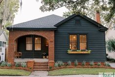 a black house with red brick and green shutters on the front door is shown