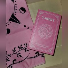 a pink tarot book laying on top of a table next to a pink scarf