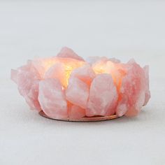 a small bowl filled with pink crystals on top of a white tablecloth next to a candle