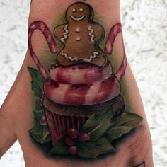 a hand tattoo with a gingerbread cupcake and candy canes on the palm