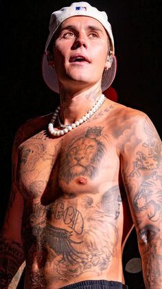 a shirtless man with tattoos on his chest and head is standing in the dark