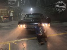 a man kneeling down in front of a car with fog coming out of it's headlights