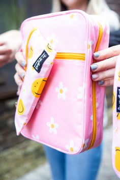 a woman holding a pink bag with yellow smiley faces on it