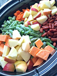 an assortment of different types of food in a crock pot with beans, apples, and carrots