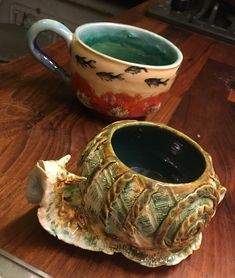 a ceramic cup sitting on top of a wooden table next to a mug filled with liquid