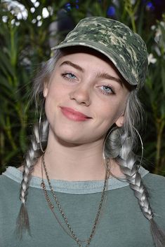 a woman with grey hair wearing a camo hat and braids in her hair