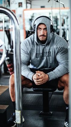 a man sitting on top of a bench in a gym wearing a hoodie and headphones