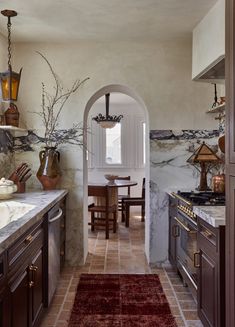 an archway leads into a kitchen with marble counter tops and wooden cabinets, along with a red rug on the floor