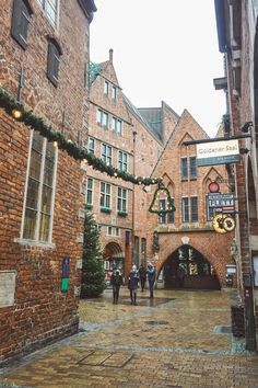 people are walking through an old brick alleyway in the city with christmas decorations on it