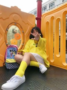 a woman sitting on top of a playground slide next to a yellow play structure and holding her hand up in the air